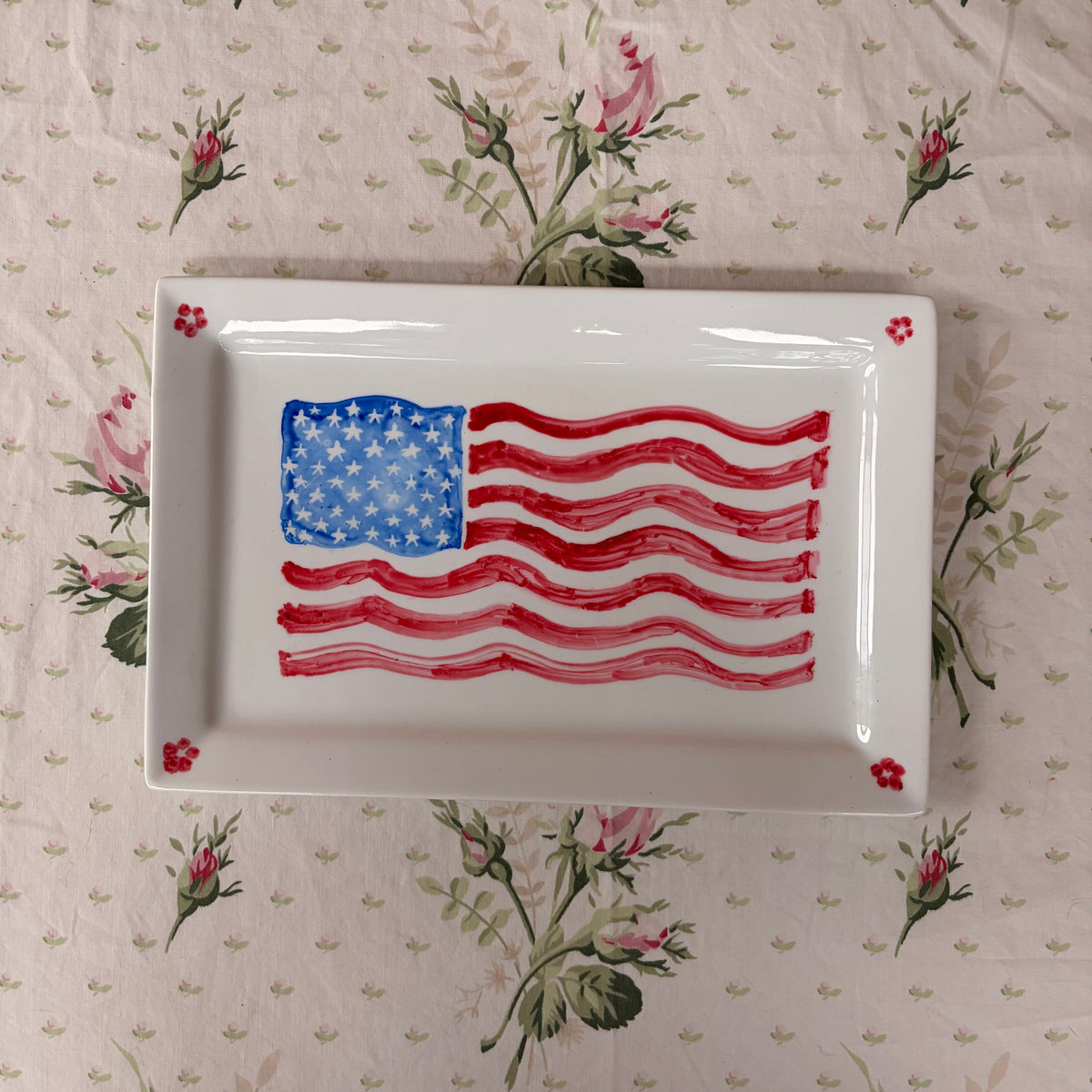 hand painted in red and blue American Flag with four red dainty flowers on a large white rectangle platter
